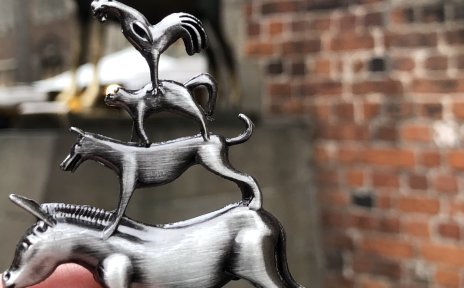 Eine Hand, die eine Metallfigur der Bremer Stadtmusikanten vor die echte Bronzefigur der Bremer Stadtmusikanten hält. Eine Hand, die eine Metallfigur der Bremer Stadtmusikanten vor die echte Bronzefigur der Bremer Stadtmusikanten hält.