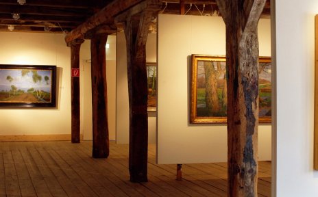 Ein Ausstellungssaal mit Gemälden, Dielenboden und Holzbalken. Ein Ausstellungssaal mit Gemälden, Dielenboden und Holzbalken.