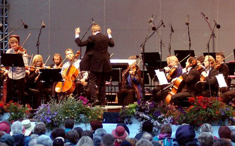 Blick durch Blätter hindurch auf eine Bühne mit einem klassischen Orchester. Davor das Publikum. Blick durch Blätter hindurch auf eine Bühne mit einem klassischen Orchester. Davor das Publikum.