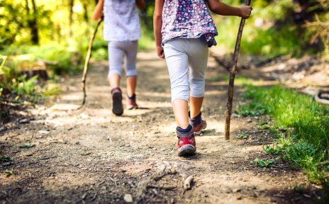 Zwei kleine Mädchen laufen mit Wanderstöcken durch einen Wald. Zwei kleine Mädchen laufen mit Wanderstöcken durch einen Wald.
