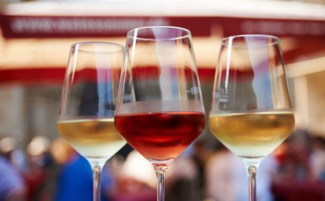 Zwei Weingläser mit einem roten und einem weißen Wein gefüllt stehen in einer Nahaufnahme vor dem Festgetümmel im Hintergrund auf einem Tisch. Zwei Weingläser mit einem roten und einem weißen Wein gefüllt stehen in einer Nahaufnahme vor dem Festgetümmel im Hintergrund auf einem Tisch.