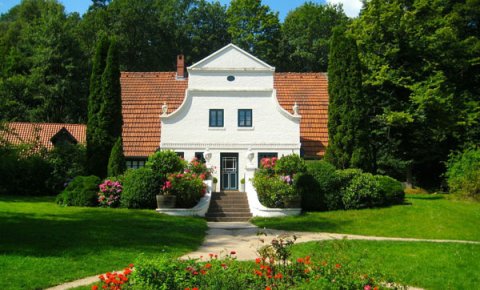 Weißes Haus mit rotem Dach umringt von Bäumen und Wiese Weißes Haus mit rotem Dach umringt von Bäumen und Wiese