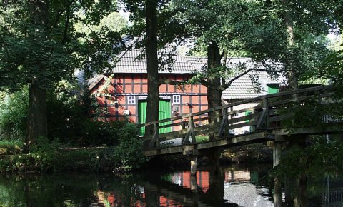 Eine hölzerne Brücke führt über einen Fluss zu einem Fachwerkhaus. Eine hölzerne Brücke führt über einen Fluss zu einem Fachwerkhaus.