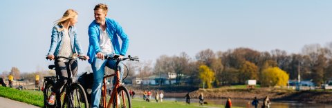 Ein junges Paar fährt Fahrrad am Deich Ein junges Paar fährt Fahrrad am Deich