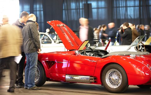 Beuscher der Bremen Classic Motorshow bestaunen einen roten Oldtimer. Beuscher der Bremen Classic Motorshow bestaunen einen roten Oldtimer.