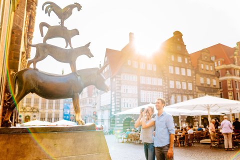 Eine Frau und ein Mann stehen vor den Bremer Stadtmusikanten. Die Frau macht von der Bronzestatue ein Bild. Eine Frau und ein Mann stehen vor den Bremer Stadtmusikanten. Die Frau macht von der Bronzestatue ein Bild.