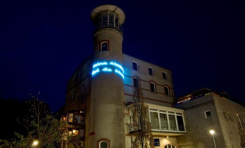 Das Gebäude der Städtischen Galerie bei Nacht, ein kleiner Turm ist mit blauer Schrift beleuchtet. Das Gebäude der Städtischen Galerie bei Nacht, ein kleiner Turm ist mit blauer Schrift beleuchtet.