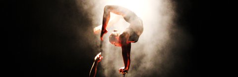 Eine Artistin macht einen Handstand auf einem schmaclen Podest und beugt Beine und Kopf Richtung Rücken Eine Artistin macht einen Handstand auf einem schmaclen Podest und beugt Beine und Kopf Richtung Rücken