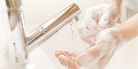 Mit Seife eingeseifte Hände neben einem laufenden Wasserhahn Mit Seife eingeseifte Hände neben einem laufenden Wasserhahn