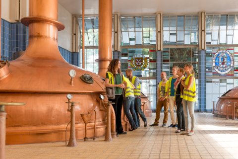 Eine kleine Gruppe steht neben zwei großen Sudkesseln. Eine kleine Gruppe steht neben zwei großen Sudkesseln.