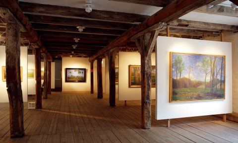Ein Ausstellungssaal mit Gemälden, Dielenboden und Holzbalken. Ein Ausstellungssaal mit Gemälden, Dielenboden und Holzbalken.