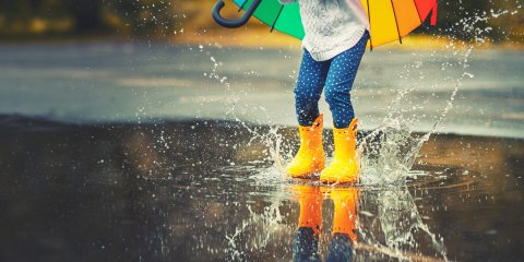 bunt gekleidete Beine springen mit gelben Gummistiefel in eine Pfütze. bunt gekleidete Beine springen mit gelben Gummistiefel in eine Pfütze.