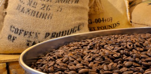Geröstete Kaffeebohnen, im Hintergrund Kaffeesäcke Geröstete Kaffeebohnen, im Hintergrund Kaffeesäcke