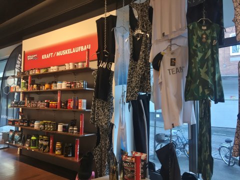 Sportklamotten hängen an der Wand und verschiedene Sportlernahrung steht im Regal. Sportklamotten hängen an der Wand und verschiedene Sportlernahrung steht im Regal.