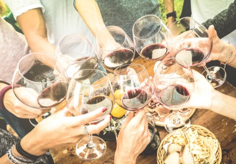 Freunde stoßen mit Rotwein an einem gedeckten Tisch an Freunde stoßen mit Rotwein an einem gedeckten Tisch an