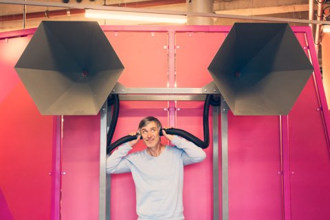 Ein Mann vor pinker Wand mit zwei Rohren an den Ohren Ein Mann vor pinker Wand mit zwei Rohren an den Ohren