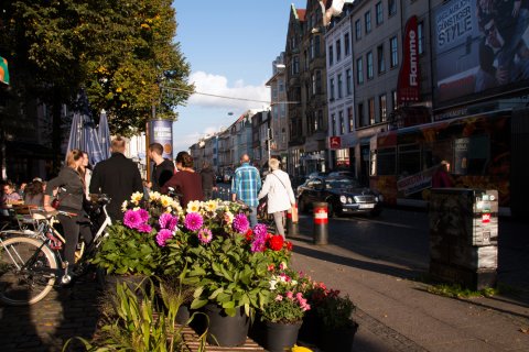 Menschen treffen sich im Viertel, im Vordergrund bunte Blumen eines Blumenstandes Menschen treffen sich im Viertel, im Vordergrund bunte Blumen eines Blumenstandes