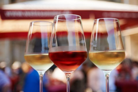 Zwei Weingläser mit einem roten und einem weißen Wein gefüllt stehen in einer Nahaufnahme vor dem Festgetümmel im Hintergrund auf einem Tisch. Zwei Weingläser mit einem roten und einem weißen Wein gefüllt stehen in einer Nahaufnahme vor dem Festgetümmel im Hintergrund auf einem Tisch.