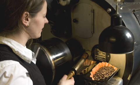 Eine Frau nimmt Kaffeebohnen aus einer großen Maschine. Eine Frau nimmt Kaffeebohnen aus einer großen Maschine.